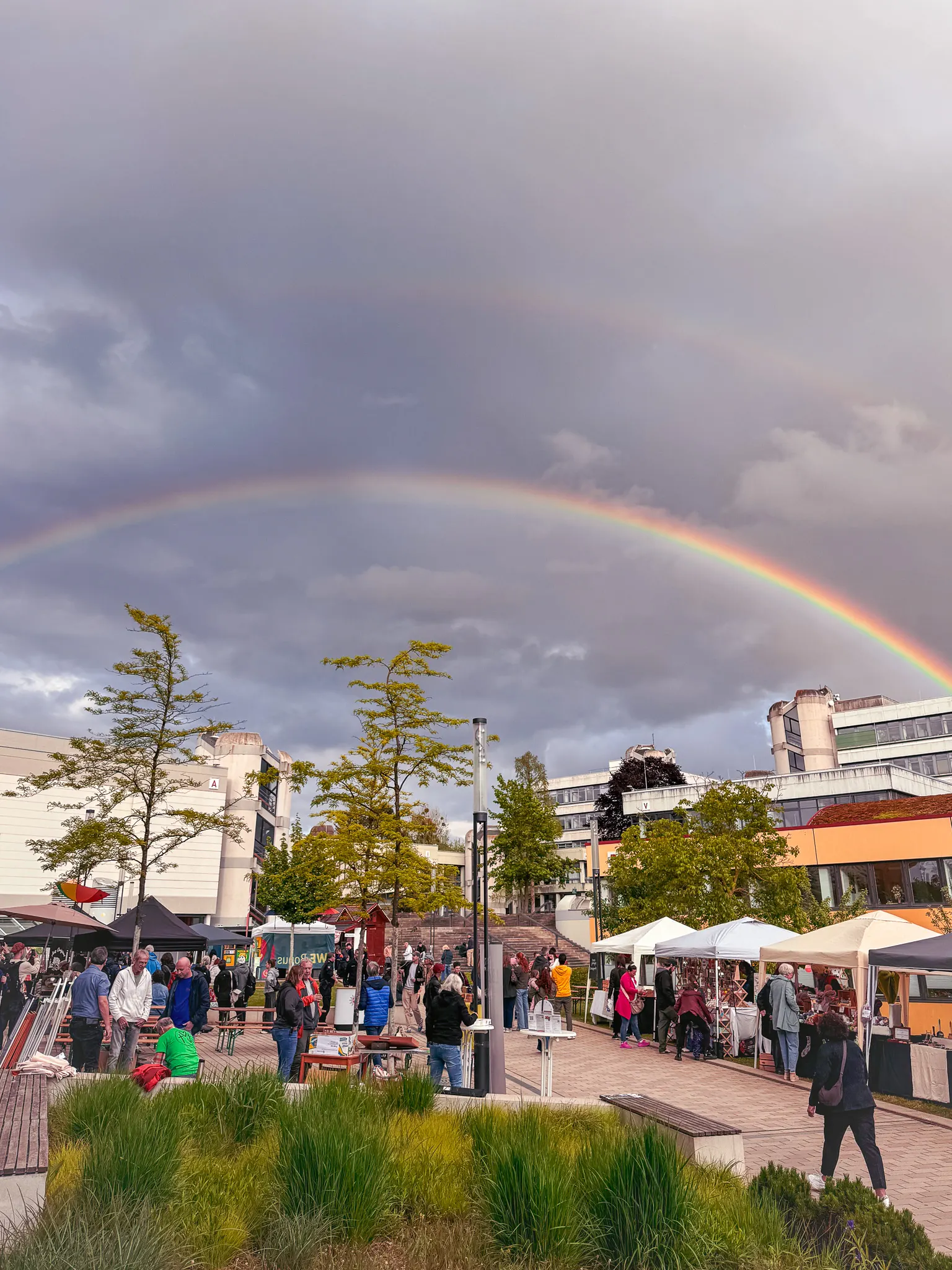 Feierabendmarkt mit Ständen und Besuchern unter einem Regenbogen bei bewölktem Himmel in Hildesheim